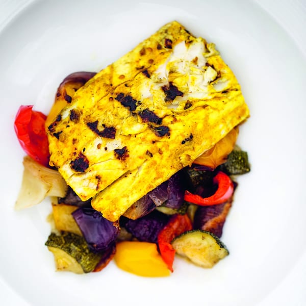 Indian grilled paneer with charred red peppers, zucchini, and purple onions on a white plate.