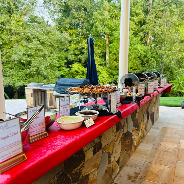 An outdoor Indian food buffet from Bazil Indian Cuisine with various dishes and chutneys on a stone counter.