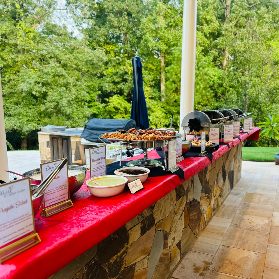 An outdoor Indian food buffet from Bazil Indian Cuisine with various dishes and chutneys on a stone counter.